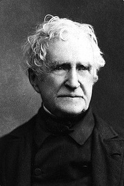 Black-and-white portrait photograph of an old white man with wavy white hair and wearing a black coat