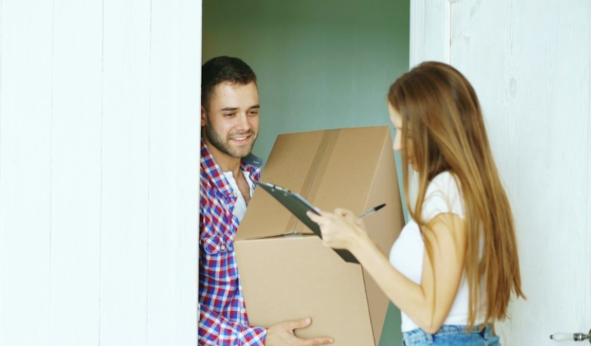 Photo by Vitaly Gariev on Unsplash Alt text: A courier holds a cardboard box while a woman signs his clipboard at the door