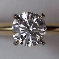 A clear faceted gem supported in four clamps attached to a wedding ring