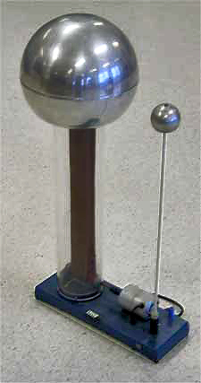 Large metal sphere supported on a clear plastic column, inside of which a rubber belt can be seen. A smaller sphere is supported on a metal rod. Both are mounted to a baseplate, on which there is a small driving electric motor.
