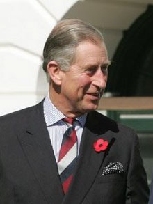 Head and shoulders shot of Prince Charles dressed in a grey suit with a poppy pinned to the left lapelle, blue shirt and red, white and blue striped tie.