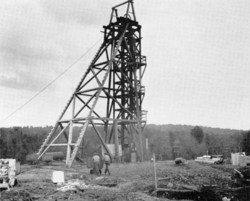A wooden frame above the mine's shaft, two men pushing a small cart on tracks