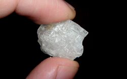A shiny translucent white crystal of methamphetamine, held between the ends of a finger and thumb