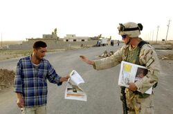 US Army soldier hands out a newspaper to a local Aug 2004.jpg
