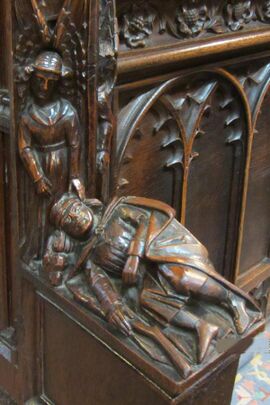 A wooden carving shows a woman attending a man who is lying on the ground with a crutch