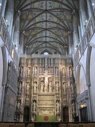 The photo shows the altar of St. Alban's Cathedral, behind which rises a large stone screen with tiers of statues, and a crucifix, centrally placed.