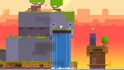 Gomez stands atop an anthropomorphic, purple structure with water falling from its orifices, as if it were crying. Trees grow atop the structure, grass lines the platforms, and the background is a deep blue to orange gradient of a sunset. A bomb sits alone on the left side of the screen.