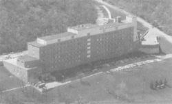 A black-and-white aerial photograph of a long, narrow six-story building