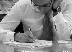 A man in a formal shirt and tie writes in a notebook