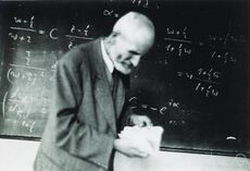 Oskar Perron reading a book while standing in front of a blackboard containing equations