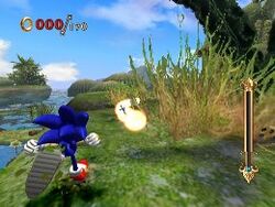 The hedgehog runs up a grassy hill which veers off to the right, partially obscured by a bush. He prepares to run into a trail of bright spheres resembling pearls. The area overlooks a swamp and the deep daytime sky.