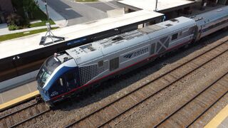 Gray diesel locomotive with a red sill stripe. The area around the cab windows is black. The sides of the cab are blue, tapering with halftone dots onto the side of the body.