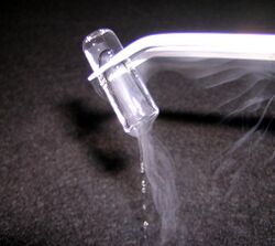 a glass tube, held upside down by some tongs, has a clear-looking ice-like plug in it which is slowly melting judging from the clear drops falling out of the open end of the tube