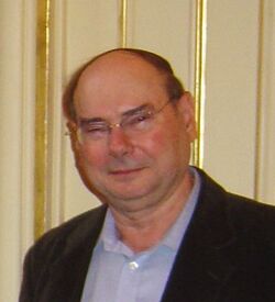 Portrait of an Israeli man in his sixties. His hair is short and balding, and he is wearing glasses with a dress shirt and jacket.