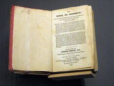 A photograph of the 1841 First European (London) edition of the Book of Mormon. It is open to its title page. The edges of the page are colored red.