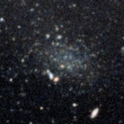 Photograph of a small, faint galaxy appearing as a smudge in the centre of a starfield