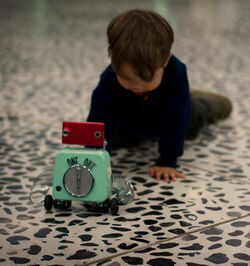 A child appears to crawl toward a tiny toy robot