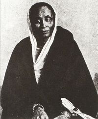 An elderly Bengali woman in white sati and a dark wrapper