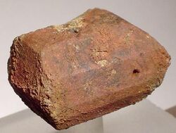 Terracotta coloured prism-shaped crystal, rough texture, seems to have about ten sides