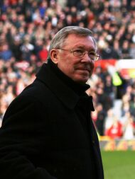 The torso and head of a grey-haired white man. He is wearing spectacles and a black coat.