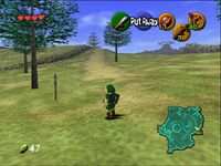 The child version of the game's protagonist, Link, stands in Hyrule field wearing his distinctive green tunic and pointed cap. In each corner of the screen are icons that display information to the player. In the upper left-hand corner, there are hearts, which represent Link's health, in the lower left-hand corner is a counter that displays the number of Rupees (the in-game currency) possessed by the player. There is a mini-map in the lower right-hand corner, and five icons in the upper right-hand corner, one green, one red, and three yellow, which represent the actions available to the player on the corresponding buttons of the N64 controller.