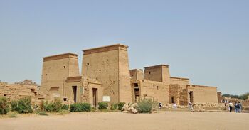 Stone building fronted by a tall gateway, a colonnade, and another gateway