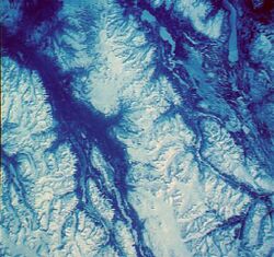 An overhead view of snow-covered mountains with intervening river valleys.