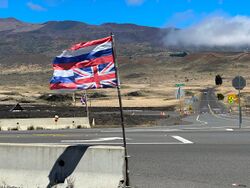 An inverted Hawaiian flag in the foreground, in the background the saddle road and behind it a road up Mauna Kea