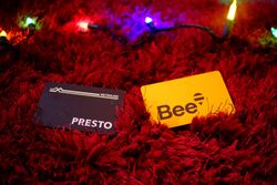 photograph of fare cards on a red fluffy carpet, with multicoloured fairy lights in the background. the mood is warm and dark. the cards are a black presto card, and a yellow bee card