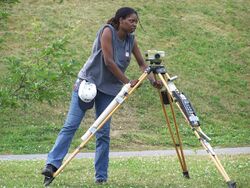 A woman setting up an optical level on a tripod.