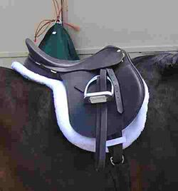 An English saddle set on top of a white pad that has the same shape as the saddle