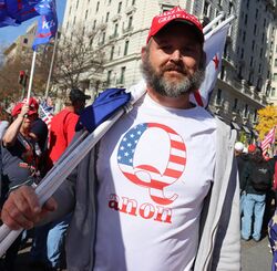 Man wearing a t-shirt with a design consisting of a block letter "Q" overlaid with an American flag pattern