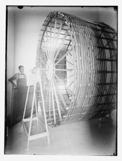 a man stands in a corner observing film strips that have been wrapped around a giant wooden wheel to dry them