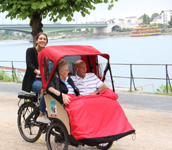 A young lady drives a trishaw with two elderly persons along the Rhine river near Bonn, Germany