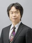 A 67-year-old Japanese man with graying black hair and a suit, looking towards the camera.