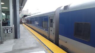 Gray passenger rail cars with a wide blue window stripe