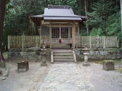 An image of Takijiri-oji shrine, the formal entryway into the holy land of Kumano. It is a wooden shrine building with stone lanterns in the front set against forested mountains.
