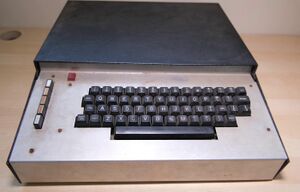 An image of the Transam Triton home computer resting on a desk. The picture shows a keyboard in a long metal case with five function buttons to the left.