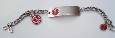 A metal bracelet, engraved with a short list of important medical information, and decorated with a red symbol representing medicine