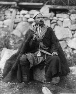 A seated man, in traditional garb, smoking a pipe
