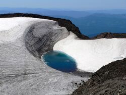 A small pool of water in a snowfield with other peaks in the mist receding in the distance
