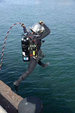 A surface supplied diver entering the water with a diver's umbilical laid up from differently coloured twisted hoses and cables leading back to the boat