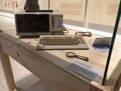 An old computer, accompanied by a pair of glasses and a loupe.
