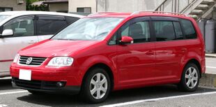 Front-three-quarter view of a five-door car with a raised roofline, flush headlights, front foglamps, door mirrors with integrated turning indicator lights, alloy wheels, and bars for attaching a roof rack