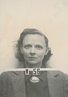 Mug shot of woman with glasses in suit The number V-56 appears in front of him.