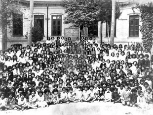 A black-and-white photograph of several dozen girls seated in front of a school building