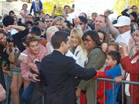 Tobey Maguire, in a suit, greets fans behind a security barrier. Most of the attendants hold cameras.