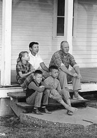 A black and white photograph of two parents and three children sitting on a porch.