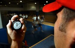 US Navy 030506-N-5862D-128 An instructor in the Freedom Hall athletic complex uses a stopwatch while recruits run a 1.5-mile track during a Physical Fitness Test (PFT).jpg