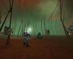 An armored man holding a sword-like object standing in a large, foggy room filled with thick strands extending from floor to ceiling. Three floating creatures and one dead creature surround him.